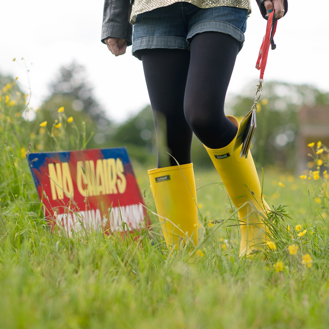 Close up image of a woman wearing a pair of yellow Cotswold wellingtons in a festival setting