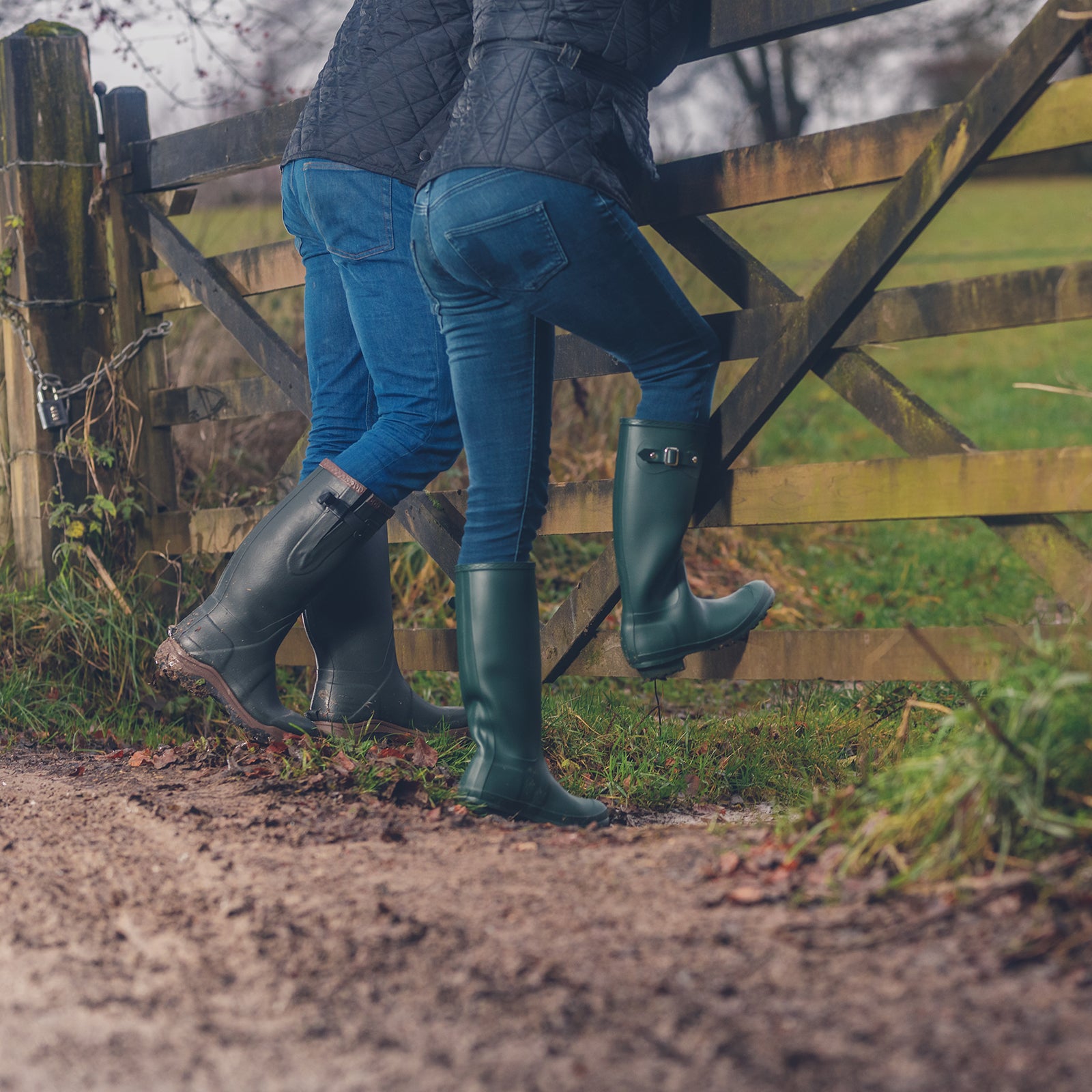 Two people leaning on a gate, wearing Cotswold wellingtons