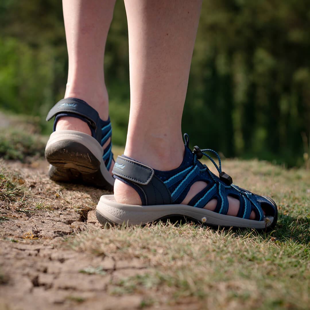 Close-up image of a woman wearing a pair of navy Cotswold Upton Sandals outside.