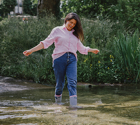 Woman walking through a stream, wearing a pink shirt, jeans and a pair of Cotswold wellingtons