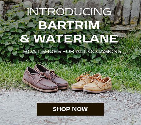 Brown and tan coloured Cotswold Bartrim & Waterlane boat shoes on a roadside with nettles behind. Text reads 'INTRODUCING BARTRIM & WATERLANE. BOAT SHOES FOR ALL OCCASIONS. SHOP NOW'