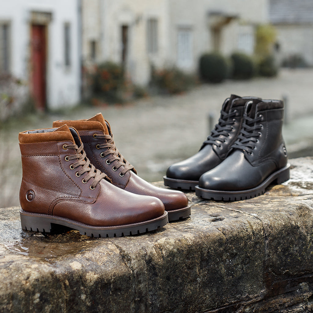 A pair of brown and black Thorsbury boots on a wet wall with a row of out of focus houses behind