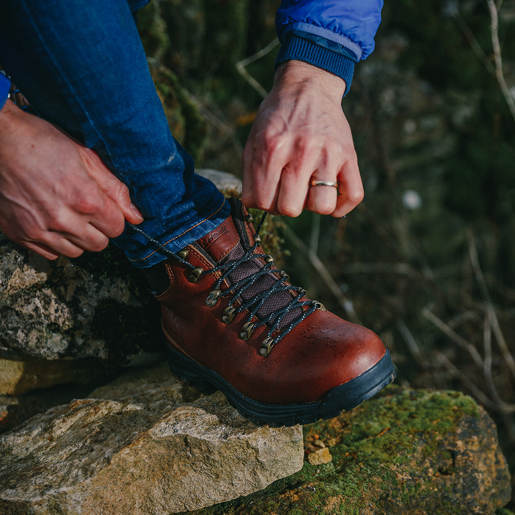 Man tying up a brown Cotswold Kingsway Hiking Boot on mossy rocks