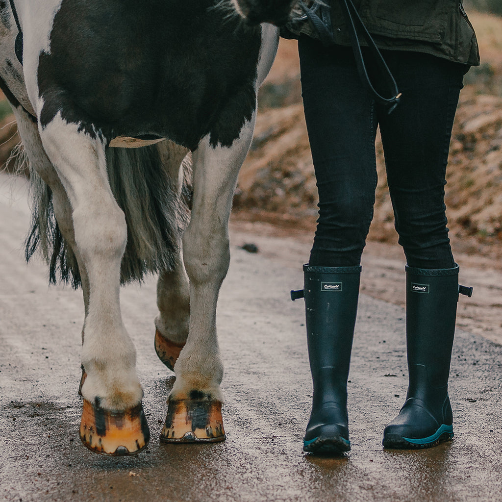 Woman wearing a pair of Cotswold Realm Adjustable Wellingtons, stood next to a horse