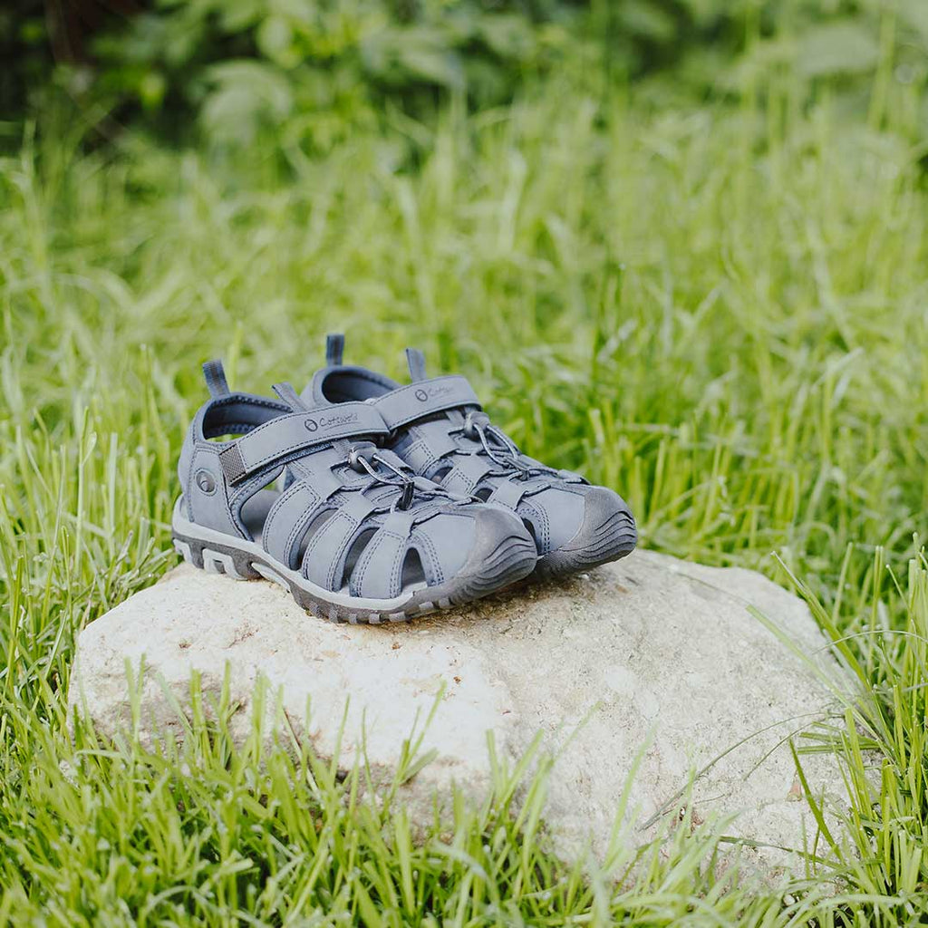 A pair of navy Cotswold Furz sandals on a rock in long grass